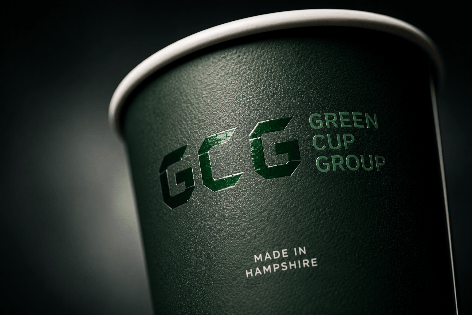 Green Cup brand illustration: light catches the glossy GCG mark on a textured dark-green cup beneath its ivory rim.